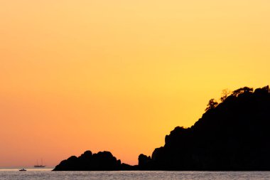 Gün batımında ağaçlarla birlikte deniz kıyısının silueti. Sahilde yaz günbatımı