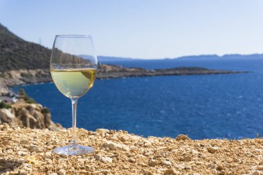 Bir bardak beyaz şarap. Deniz kıyısının arka planında şarap ve güneşli bir yaz plajı. Tatil köyünde şarap tatma ve rahatlama.