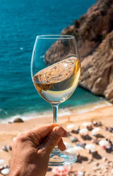 A glass of white wine in a man\'s hand. Wine against the backdrop of the sea coast and a sunny summer beach. Wine tasting and relaxation at the resort