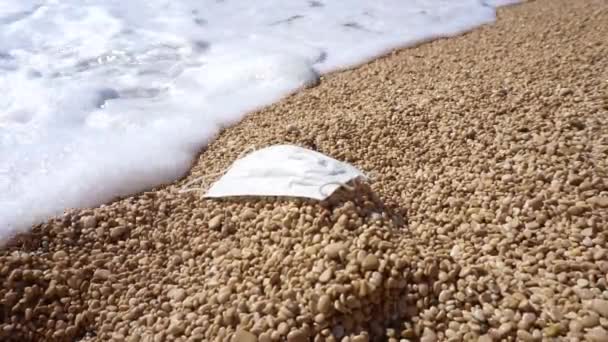 Máscara de protecção médica lançada numa praia de mar vazia. Poluição ambiental com máscaras médicas contra o coronavírus. Conceito de resíduos de máscara — Vídeo de Stock