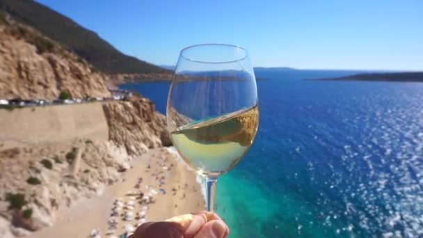 Vino blanco en una copa sobre el telón de fondo de una soleada playa de verano y mar turquesa. Mano con copa de vino y degustación — Vídeos de Stock