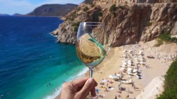 Vin blanc dans un verre sur fond de plage ensoleillée et de mer turquoise. Main avec verre de vin et dégustation — Video