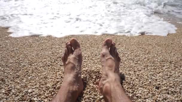 Pies masculinos en la arena bajo el sol. El hombre toma el sol y se relaja en la playa del mar — Vídeo de stock