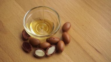 Argan yağı, ahşap zemin üzerinde argan tohumları olan cam bir kâseye konur. Argan yağı bazlı kozmetik konsepti.