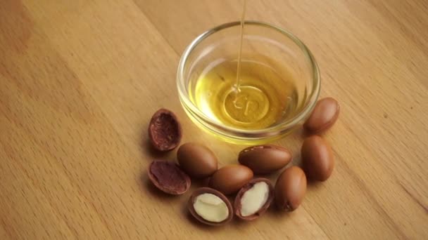 Olio di Argan in una ciotola di vetro con semi di argan su fondo di legno. Concetto cosmetico a base di olio di Argan. — Video Stock