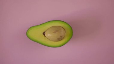 Pembe arka planda bir avokado. İzole edilmiş bir arkaplanda yarım dönen bir avokado. Yemek videosu döngüleniyor