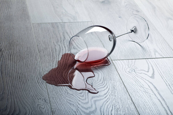 Деревянный пол с опрокинутым бокалом красного вина. Пролитое вино на деревянный ламинат (паркет) с защитой от влаги.