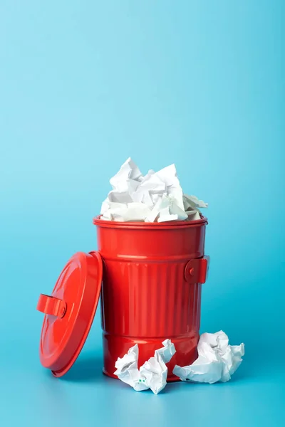 Paper trash and waste in a trash bin on a blue background. Waste and paper sorting and recycling concept