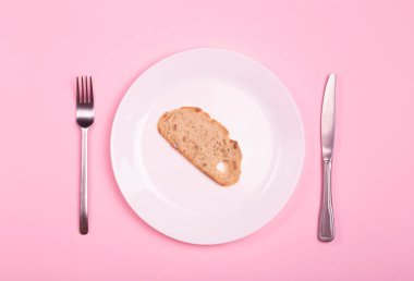 Dünya açlığı ve yoksulluk kavramı. Pembe masadaki boş tabakta bir parça ekmek..