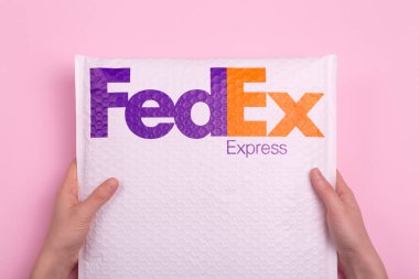 Kargo ve paket teslimatı FedEx Express ile. Pembe arka planda bir siparişi teslim eden eller.