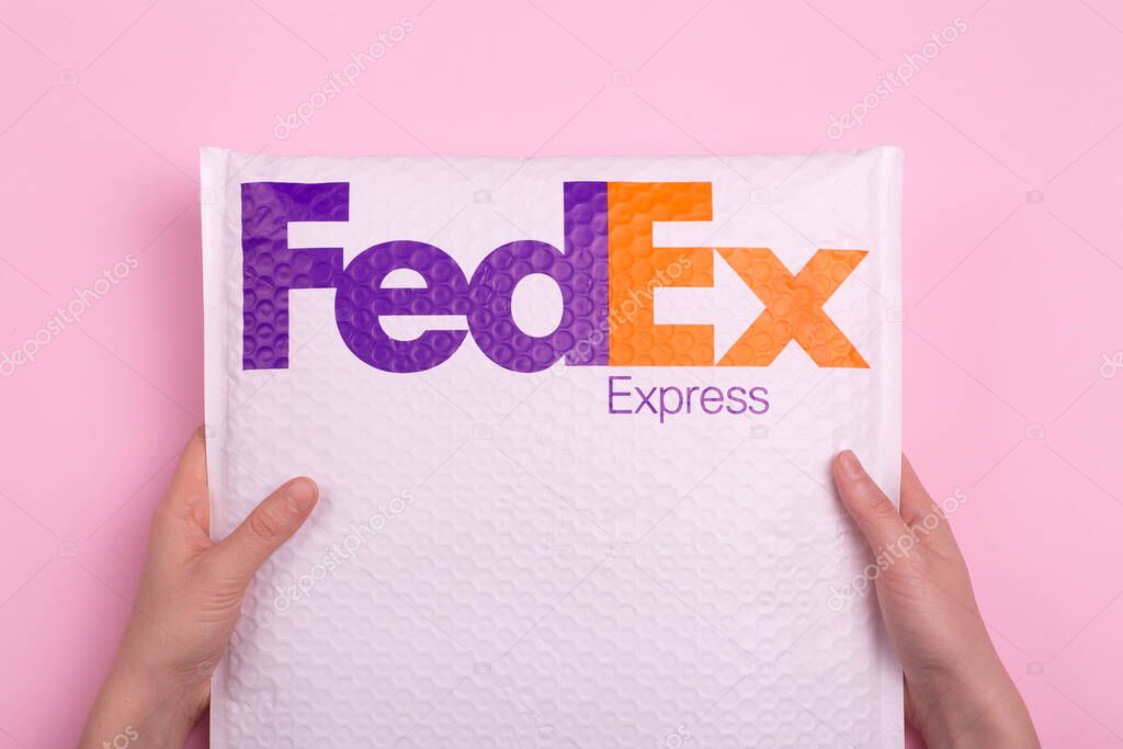 Delivery of parcels and cargo by FedEx Express. Hands delivering an order against a pink background.