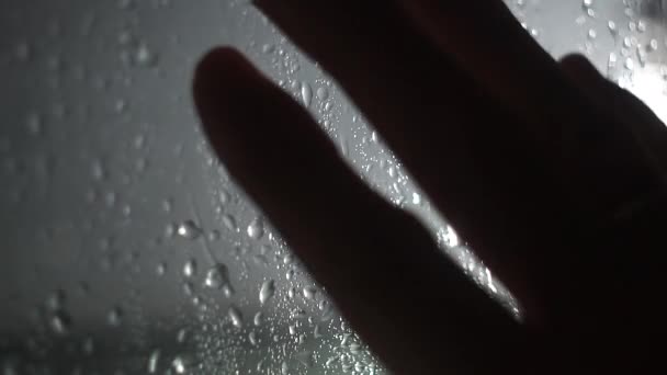 Gotas de chuva de água fluem pelo vidro com uma mão em tempo chuvoso em um fundo cinza desfocado. Textura e efeito da chuva na janela — Vídeo de Stock