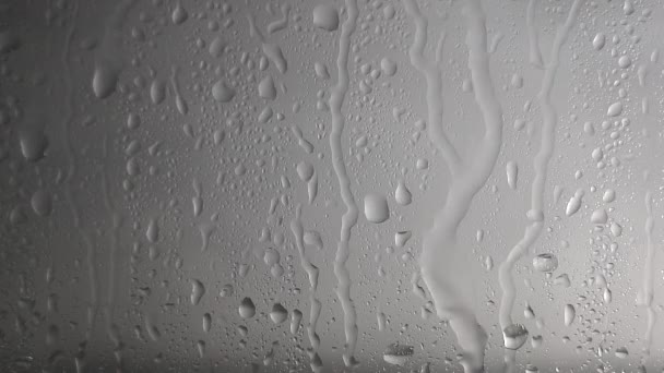 Krople wody spływają po szkle w deszczową pogodę na szarym, zamglonym tle. Tekstura i wpływ deszczu na okno — Wideo stockowe