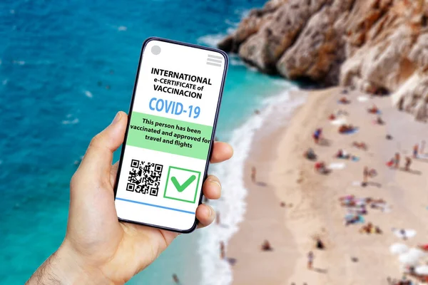 Coronavirus vaccination certificate or vaccine passport for travellers concept. COVID-19 immunity e-passport in the smartphone mobile app for international travelling. Blurred beach background
