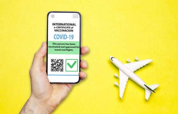 Coronavirus vaccination certificate or vaccine passport for travellers concept. COVID-19 immunity e-passport in the smartphone mobile app for international travelling. Yellow background with toy plane