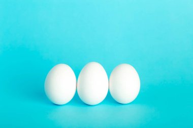 Yumurta konsepti çok az. Kahvaltının beyaz komik yumurtaları mavi bir arka planda.