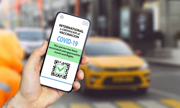 Coronavirus vaccination certificate or vaccine passport for travellers concept. COVID-19 immunity e-passport in the smartphone mobile app for international travelling. City street background
