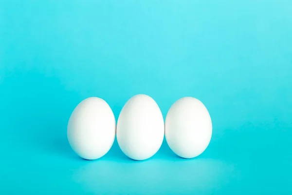 Eggs minimal concept. White funny eggs for breakfast on a colored blue background