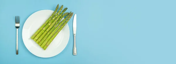 Asparagus on a white plate on a blue banner background. Fresh vegetable asparagus for a healthy diet and nutrition. Vegetables and healthy food concept — Stock Photo, Image