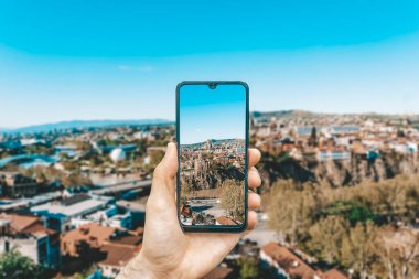 Georgia ve Tiflis manzarası. Elinde akıllı bir telefonla Georgia ve Tiflis 'in fotoğraflarını çeken bir el. Gürcistan 'da seyahat ve turizm kavramı.