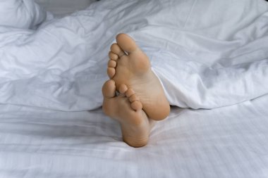 Günaydın ve uyanıyorum. Sabahları yorganın altında ayaklar. Beyaz bir yatakta yorganın altında kadın ayakları. Rahatla, uyu, dinlen konsepti.