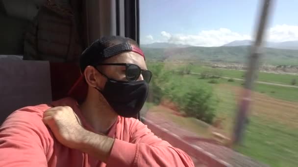 A man travels in a train carriage wearing a protective mask against the COVID-19 coronavirus during an epidemic and quarantine. A passenger in a train carriage looks out the window — Stock Video