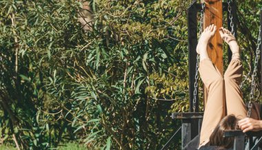 Female bare feet on a swing in the park under the sun. The girl is resting and relaxing in the summer in the park. Recreation and relaxation in nature in summer concept