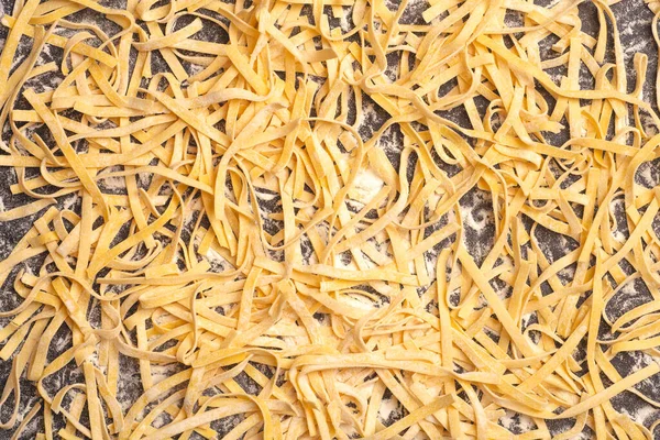 Verse pasta achtergrond. Zelfgemaakte Italiaanse fettuccine pasta gekookt in de huiskeuken met verse eieren en bloem op een houten achtergrond. Italiaans eten en keuken concept — Stockfoto