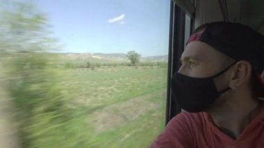 Bir adam salgın ve karantina sırasında COVID-19 koronavirüsüne karşı koruyucu bir maske takarak tren vagonunda seyahat ediyor. Tren vagonundaki bir yolcu pencereden dışarı bakar.