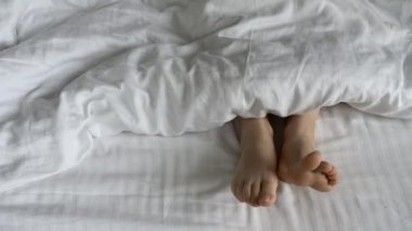 Günaydın ve uyanıyorum. Sabahları yorganın altında ayaklar. Beyaz bir yatakta yorganın altında kadın ayakları. Rahatla, uyu, dinlen konsepti.