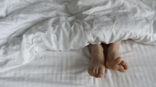 Dimineaţa şi trezirea. Picioarele sub capace în pat dimineața. Femei picioare sub capacele într-un pat alb. Relaxare, somn, conceptul de odihnă . — Videoclip de stoc