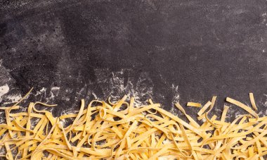 Taze makarna arka planı. Ev yapımı İtalyan fettucine makarnası. Mutfakta pişirilmiş. Ahşap zemin üzerinde taze yumurta ve un var. İtalyan yemek ve mutfak konsepti