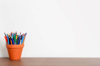 Beyaz duvarı, kalemleri ve ahşap masasında kırtasiyesi olan boş çalışma masası. Çalışma, öğrenim, okul geçmişi.