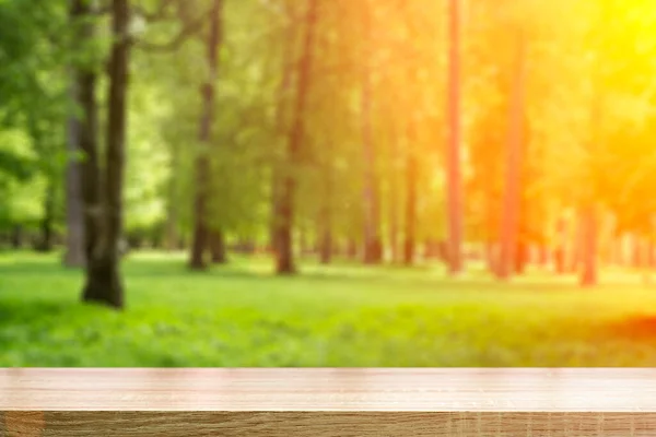 Sfondo tavolo in legno nella foresta. Sfondo di una foresta verde sfocata estiva con luce solare — Foto Stock