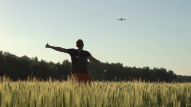 Mutlu genç adam yazın gün batımında gökyüzünde buğday tarlasında uçan bir uçağı sevinçle karşılar. Hayal, seyahat, özgürlük, mutluluk ve doğa kavramının keyfi.