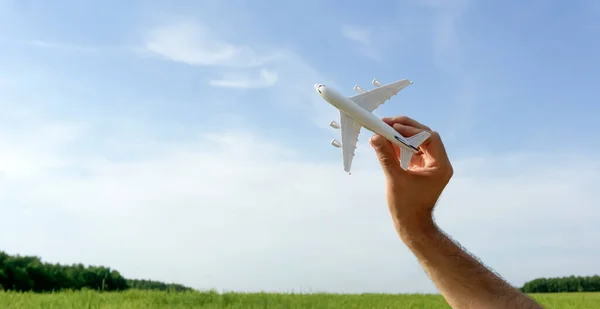 Flygplan på blå himmel banner bakgrund. Ett leksaksplan i handen flyger för att resa. Sommar, semester, resor, avkoppling, turer och flyg koncept. — Stockfoto