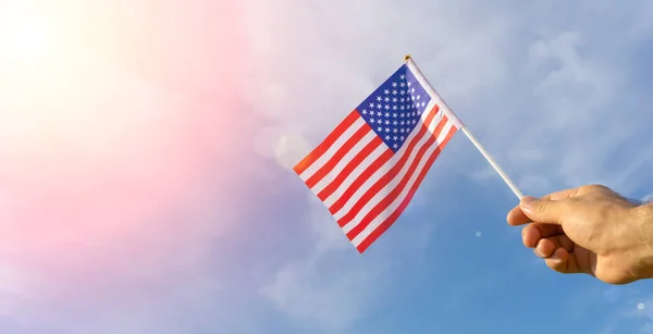 Bandeira dos EUA na mão. Bandeira festiva dos EUA na mão contra o céu azul e paisagem natural de verão. Conceito de feriados americanos. — Fotografia de Stock