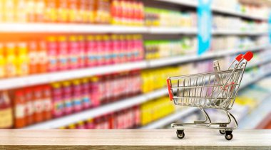 Marketin arka planında alışveriş arabası var. Yiyecek ve sebzeler raflarda bulanıklaştı..