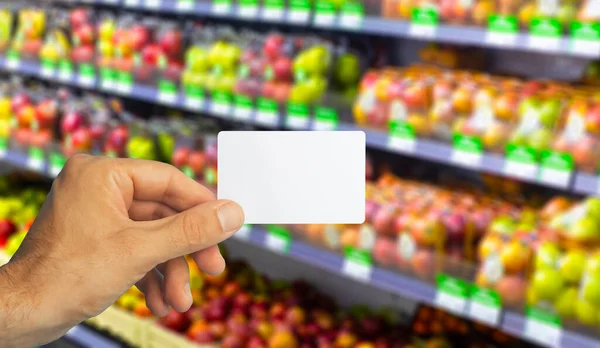 Leere Plastik-Lebensmittelkarte in der Hand auf Supermarkt-Hintergrund. Lebensmittelkarte für Rabatte und Aktionen in Geschäften und Supermärkten — Stockfoto