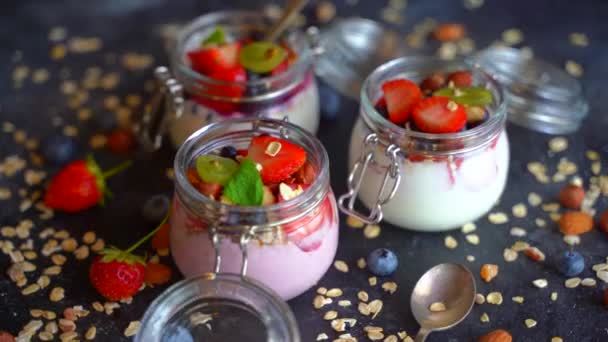 A joghurt zabmüzli és a friss bogyók az üvegekben sötét alapon forognak. Egészséges reggeli joghurttal és gyümölcsökkel.