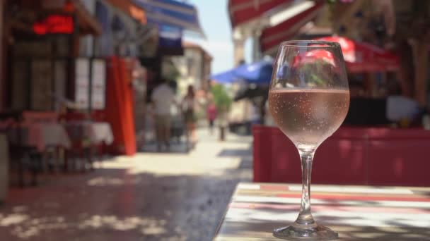 Un bicchiere di vino rosato sul tavolo di un caffè estivo in una bella strada turistica della città mediterranea. Antipasto di vino in una giornata calda. Relax video con vino — Video Stock