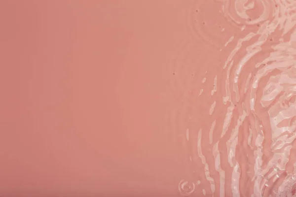 Agua tranquila ondulación de fondo. Textura de agua, círculos y burbujas en una superficie de color rosa líquido. Productos cosméticos y concepto de diseño plano — Foto de Stock