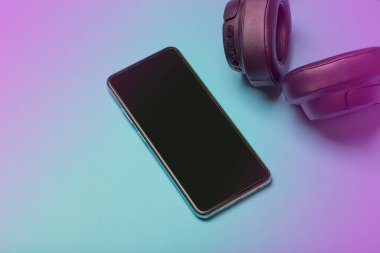 Akıllı telefonlu kulaklıklar. Renkli neon arka planda ses kulaklıkları ve boş bir akıllı telefon ekranı. Müzik uygulaması, podcast ve auobooks konsepti.