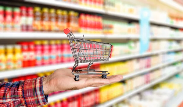 Supermarket grocery background with cart in hand. Food and groceries blurred on store shelves.