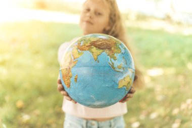 Dünya Küresi 'nden bir çocuk. İlkokul öğrencisi sarışın Avrupalı bir kızın portresi. Güneşli havalarda doğada Dünya gezegeninin eğitici bir küresi. Eğitim, eğitim, koruma ve