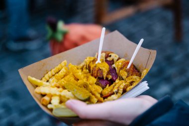 Avrupa 'da bir markette kâğıt tepside Currywurst ve patates kızartması. Bir el klasik Alman sokak yemekleriyle dolu bir kağıt tepsiyi tutar: dilimlenmiş sosis, patates kızartması ve turşu.