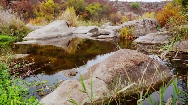 Alberi autunnali e grandi massi di pietra intorno. Una cascata d'acqua in autunno torrente con foglie cadute. L'acqua scorre intorno alle pietre nel fiume. Aktovsky Canyon, Ucraina. — Video Stock