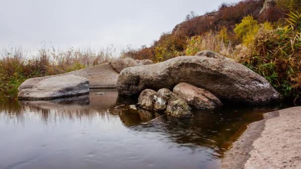 Etrafta sonbahar ağaçları ve büyük taş kayalar var. Sonbahar deresinde dökülen yapraklarla dolu bir şelale. Nehirdeki taşların etrafında su akıyor. Aktovsky Kanyonu, Ukrayna. — Stok video