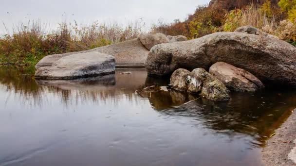 Alberi autunnali e grandi massi di pietra intorno. Una cascata d'acqua in autunno torrente con foglie cadute. L'acqua scorre intorno alle pietre nel fiume. Aktovsky Canyon, Ucraina. — Video Stock