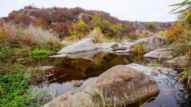 Etrafta sonbahar ağaçları ve büyük taş kayalar var. Sonbahar deresinde dökülen yapraklarla dolu bir şelale. Nehirdeki taşların etrafında su akıyor. Aktovsky Kanyonu, Ukrayna.